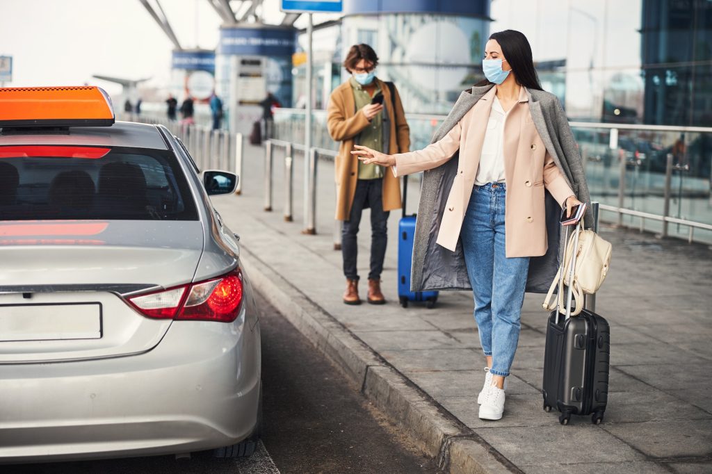 Stylish woman in medical mask catching cab at airport